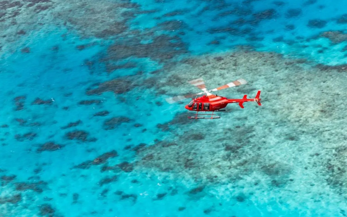 A red helicopter flying low over turquoise reef water