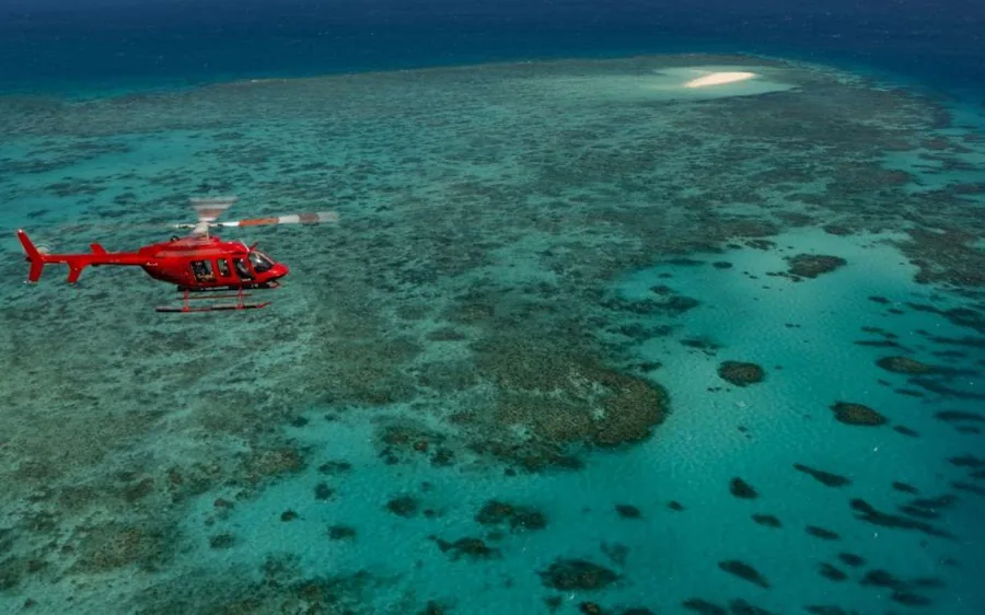 A red helicopter flying low over turquoise reef water