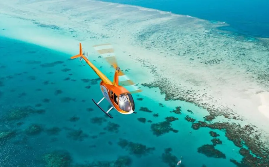 An orange helicopter over the shallow coral of the reef