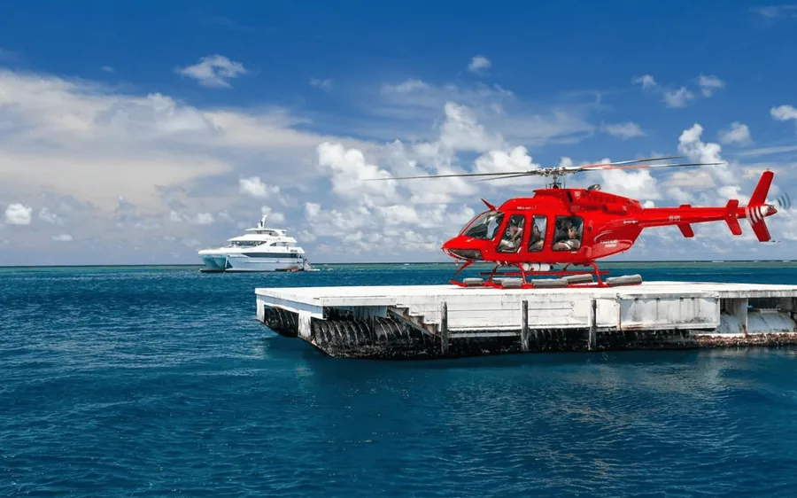 A red helicopter on a reef pontoon with the Coral Sea behind